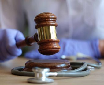 Close-up of female doctor with judge gavel and medical stethoscope. Medical litigation or verdict concept