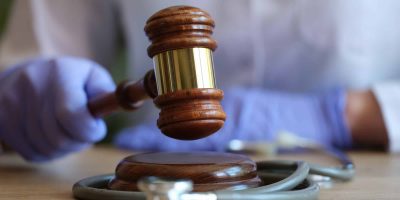 Close-up of female doctor with judge gavel and medical stethoscope. Medical litigation or verdict concept