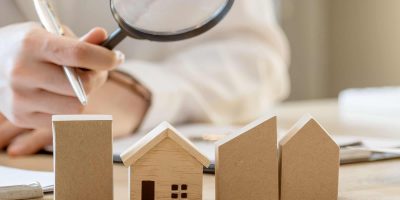 Looking for real estate agency, property insurance, mortgage loan or new house. Woman with magnifying glass over a wooden house at her office